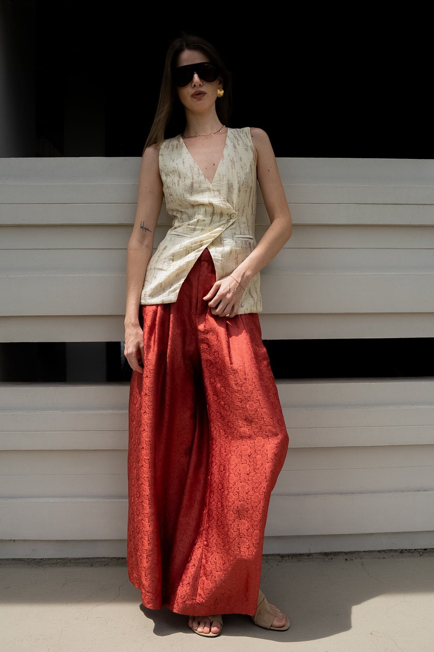 Woman wearing a sleeveless top and red pants against a white wall.